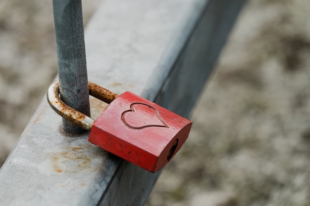 Close de um cadeado de metal com um coração pendurado em uma cerca