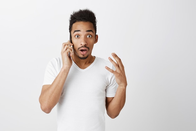 Close de um cara afro-americano surpreso falando ao telefone e parecendo surpreso