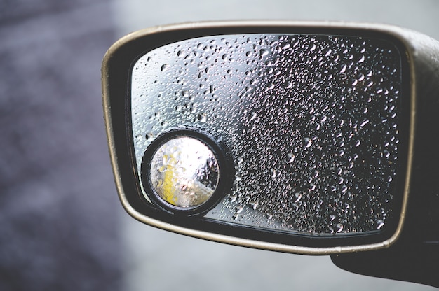 Close de um espelho retrovisor coberto de gotas de chuva sob a luz do sol