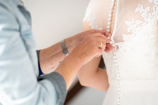 Close de um homem ajudando a esposa com um vestido de noiva