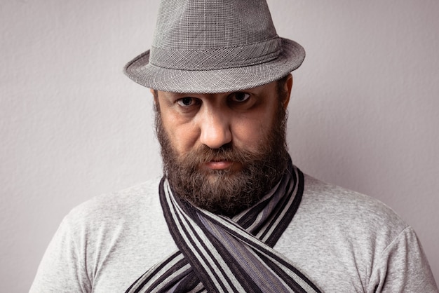 Foto grátis close de um homem barbudo vestindo uma camiseta cinza claro, chapéu e lenço em um fundo cinza