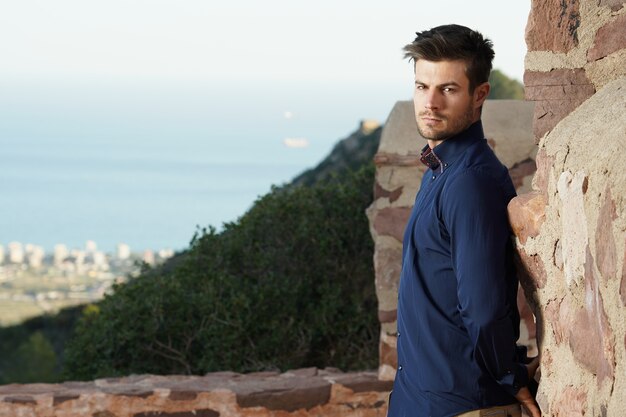 Close de um homem bem sucedido posando na frente de sua casa com uma vista perfeita da cidade atrás