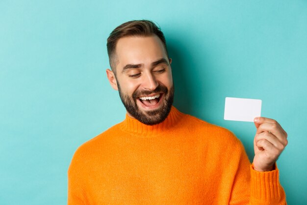 Close de um homem bonito e caucasiano, mostrando o cartão de crédito e sorrindo