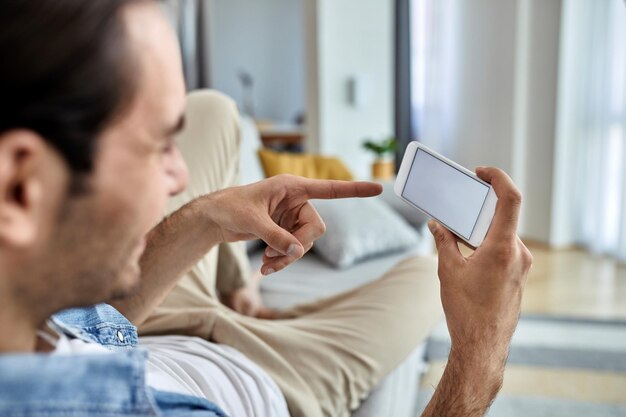 Close de um homem usando telefone celular e apontando algo na tela enquanto relaxa no sofá