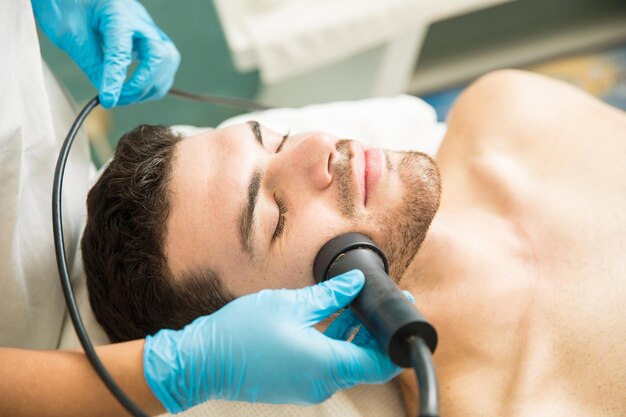 Close de um jovem bonito recebendo terapia de rejuvenescimento facial em um spa de saúde