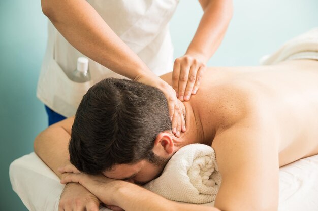 Close de um jovem recebendo uma massagem no pescoço em uma clínica de terapia e spa