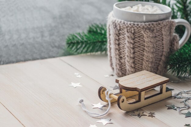 Close de um ornamento de trenó de madeira com uma caneca de marshmallows na mesa de madeira