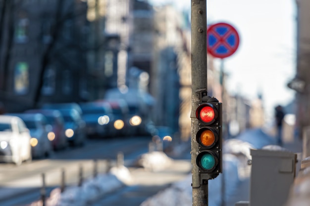 Close de um pequeno semáforo de trânsito com luz vermelha em contraste com o trânsito da cidade