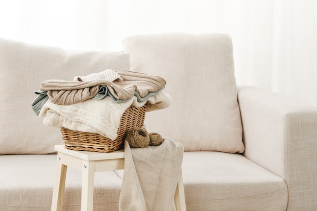 Close de um sofá cinza com uma cesta de roupas dobradas em uma pequena mesa perto dele