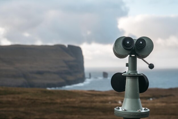 Close de um visualizador de torre no chão cercado por falésias e o mar sob um céu nublado