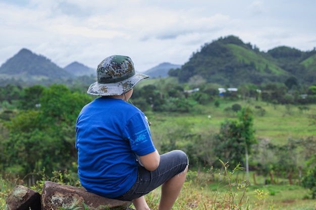 Close de uma criança sentada em uma pedra com vista para as colinas e montanhas