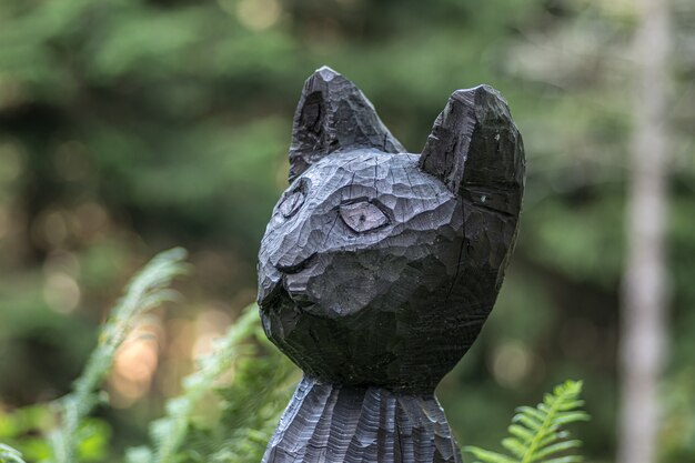 Close de uma estátua de gato preto de madeira em um campo sob a luz do sol com um fundo desfocado