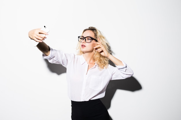 Close de uma linda mulher de negócios lúdica fazendo selfie na parede branca isolada