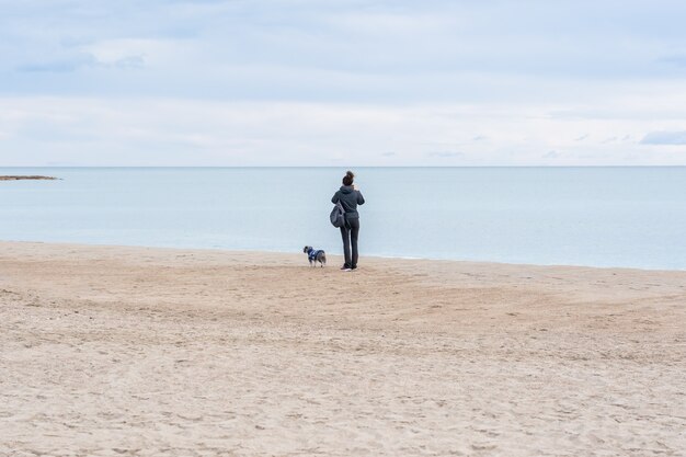 Close de uma mulher com seu cachorro em uma praia e observando a bela vista