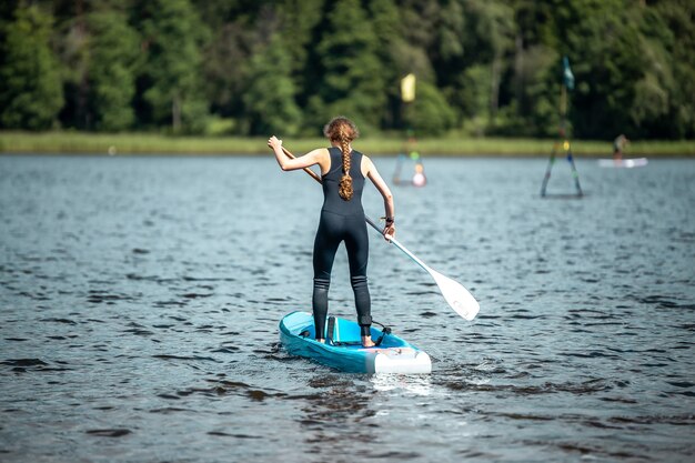 Close de uma mulher em um terno esportivo preto remando em um lago em uma competição de sup