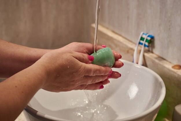 Close de uma mulher lavando as mãos com uma barra de sabão sob as luzes em um banheiro