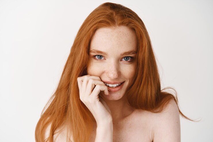 Foto grátis close de uma mulher ruiva sedutora com pele pálida e sem maquiagem, roendo a unha e olhando para a frente tentada, em pé na parede branca nua