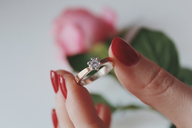 Close de uma mulher segurando um anel de diamante de ouro com uma rosa rosa