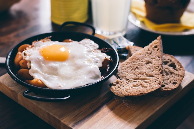 Close de uma refeição composta de ovo, torrada e feijão em uma placa de madeira