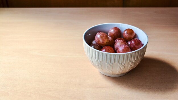 Close de uvas em uma tigela pequena sobre uma mesa de madeira