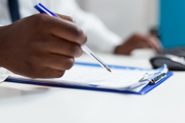 Close do médico do terapeuta americano africano analisando a papelada da prescrição do medicamento, monitorando a experiência do paciente com doença. Médico homem trabalhando em tratamento de saúde em consultório de hospital