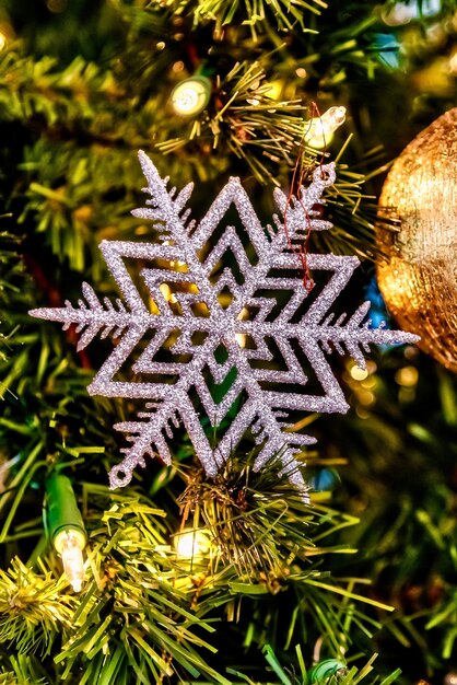 Close lindo de um floco de neve branco e outras decorações em uma árvore de Natal com luzes