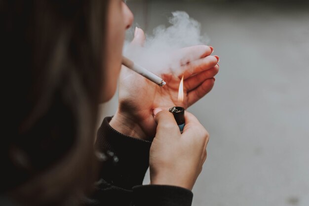 Close seletivo de uma mulher acendendo um cigarro com um isqueiro