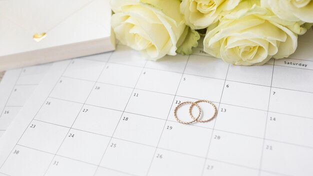 Close-up da caixa de presente; rosas e anéis de casamento no calendário