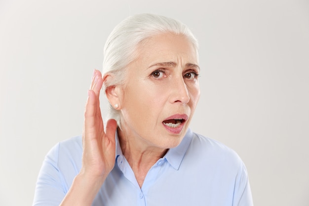 Close-up da encantadora mulher idosa, segurando a mão pela orelha e lutando para ouvir algo