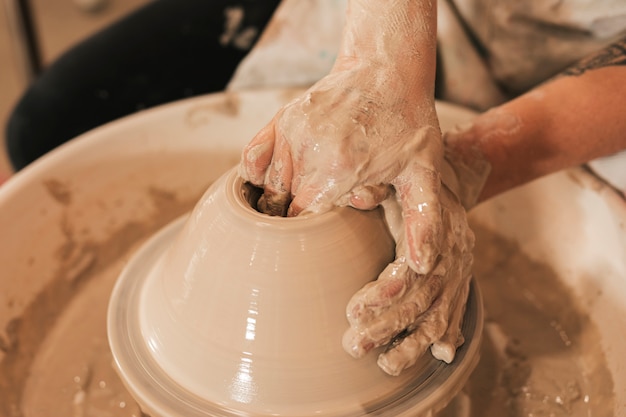 Close-up da mão do oleiro, criando um pote de barro no círculo