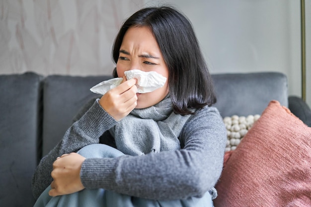 Foto grátis close-up da menina coreana espirrando em cochilo sentado em casa no cachecol sentindo-se mal conceito de inverno