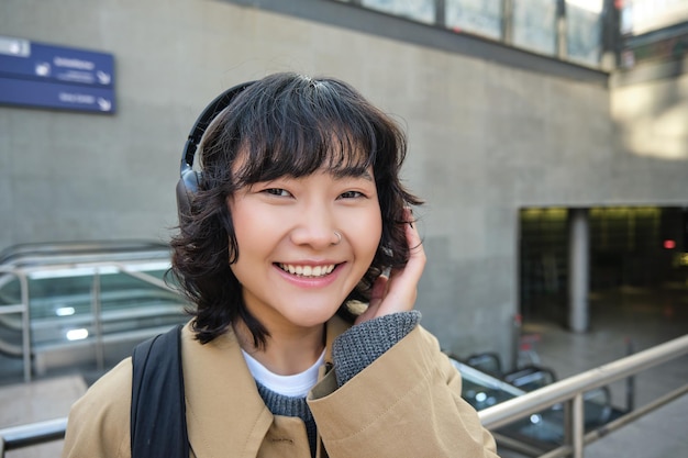 Close-up da menina morena sorridente em fones de ouvido ouve música viaja pela cidade se desloca para o trabalho