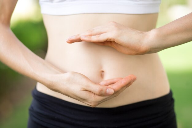 Close-up das mãos da jovem mulher e da barriga magro