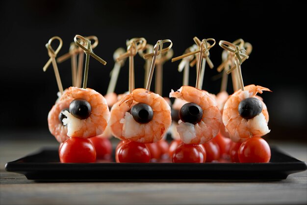 Close-up de aperitivo leve de restaurante com camarões, azeitonas pretas e cereja fresca - tomatos. Delicioso prato para um buffet ligeiro de álcool ou catering de shampagne. A foto foi tirada na parede preta