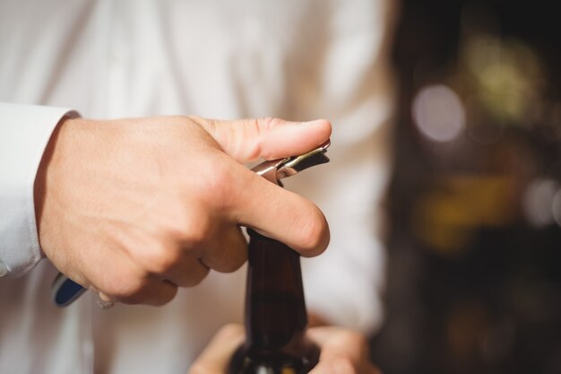 Close-up de barman, abrindo uma garrafa de cerveja