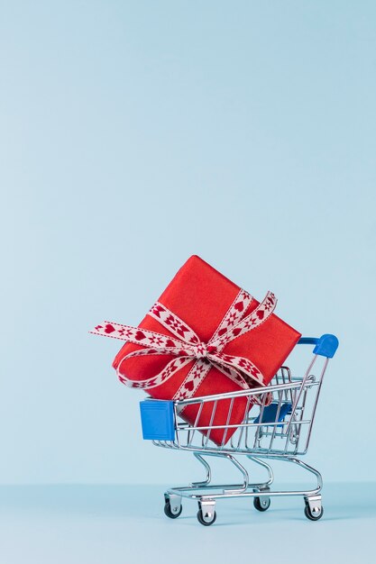 Close-up, de, embrulhado, caixa presente vermelha, em, carrinho de compras, ligado, azul, fundo