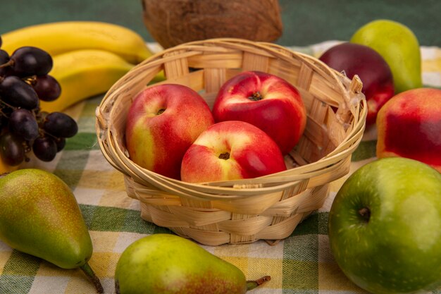 Close-up de frutas como pêssego na cesta e uva pêra banana coco em tecido xadrez sobre fundo verde