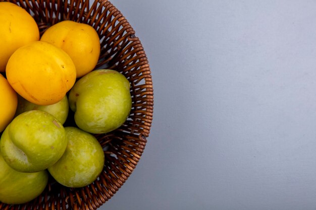 Close-up de frutas como pluots verdes e nectacots em uma cesta em um fundo cinza com espaço de cópia