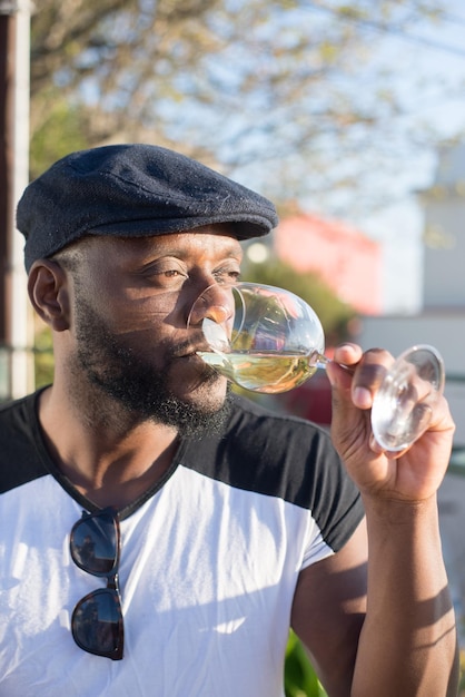 Foto grátis close-up de homem afro-americano feliz bebendo vinho. homem barbudo pensativo em roupas casuais sentado relaxado descansando desfrutando de vinho esperando a data e olhando para longe. romance, amor, conceito de namoro