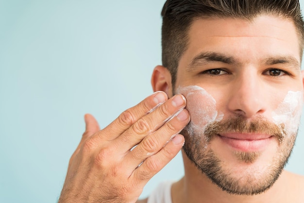 Close-up de homem atraente se preparando com creme para a pele nas bochechas no estúdio