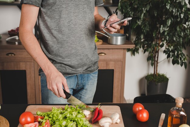 Close-up, de, homem, legumes cortantes, com, faca, usando, cellphone