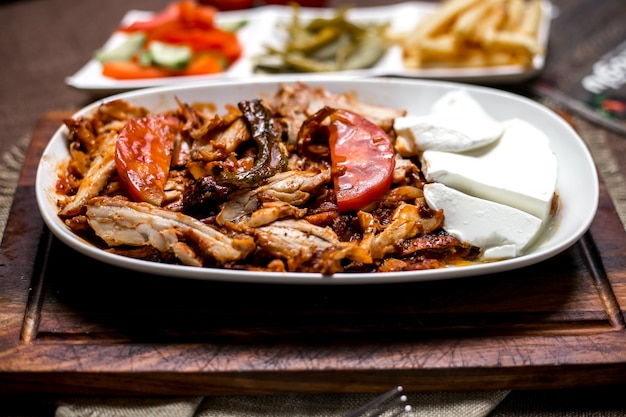 Close-up de kebab de frango com molho de tomate, servido com iogurte batatas fritas picles e legumes