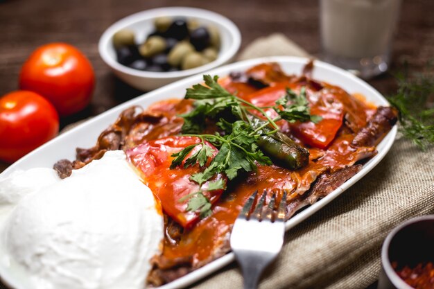 Close-up de kebab iskender, guarnecido com tomate e salsa, servido com iogurte