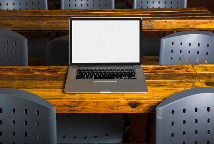 Foto grátis close-up de laptop com tela branca na mesa de madeira com cadeiras por perto