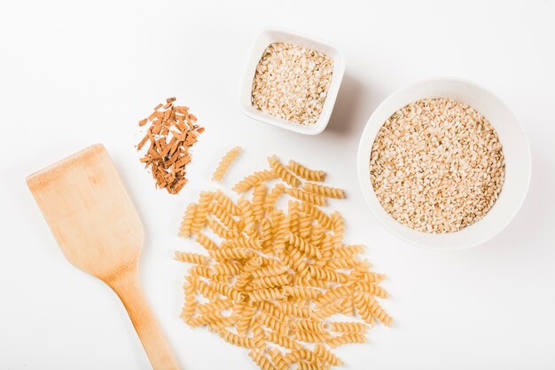 Close-up de macarrão fusilli cru; arroz e canela esmagada com espátula no fundo branco