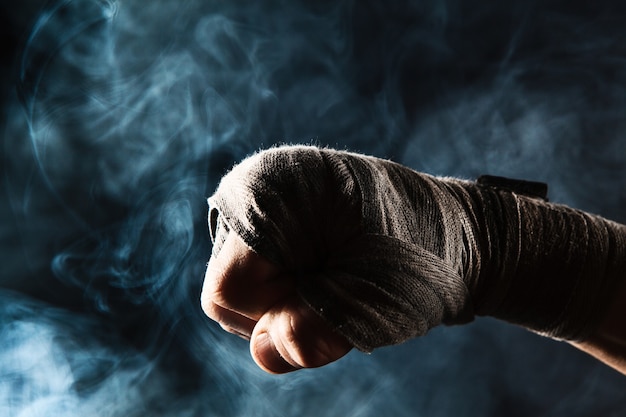 Foto grátis close-up de mão com bandagem de homem musculoso treinando kickboxing na fumaça preta e azul