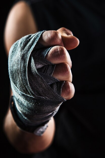 Close-up de mão com bandagem de homem musculoso treinando kickboxing no preto