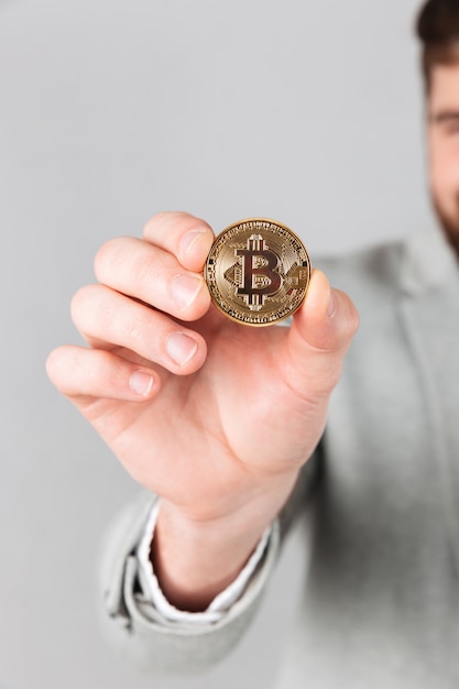 Close-up de mão masculino mostrando bitcoin dourado