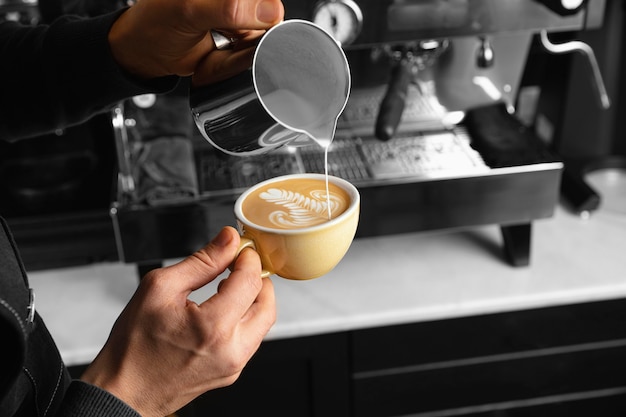 Foto grátis close-up de mão servindo leite em uma deliciosa xícara de café