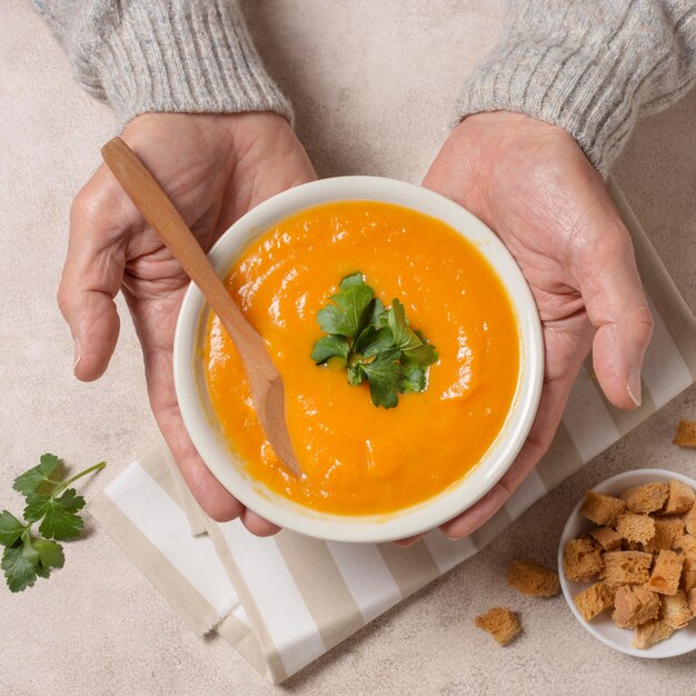 Close-up de mãos segurando uma tigela de sopa de creme